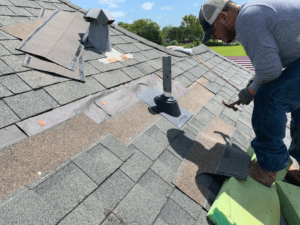 Roofing professionals inspecting damage near a vent on a suburban house