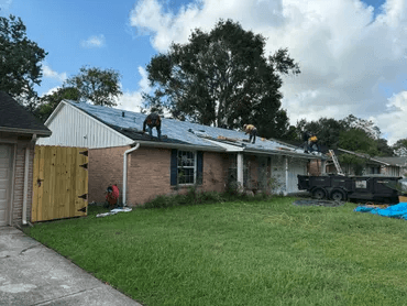 Roofer applying tarp to a storm-damaged roof during heavy winds